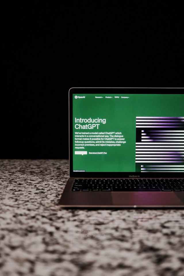 A laptop on a speckled countertop displays a website introduction for ChatGPT, featuring a green background with white text outlining its conversational abilities.