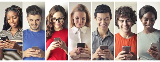 A diverse group of seven individuals, including men and women, are engaged with their smartphones, smiling and looking at their screens, set against a neutral background.
