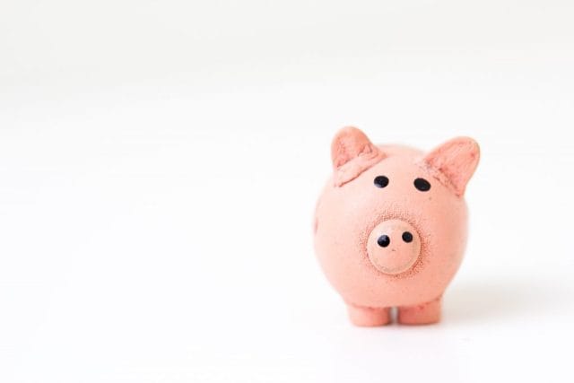 A close-up of a small, pink piggy bank on a plain white background, emphasizing its round shape and simple facial features. The piggy bank appears friendly and inviting.