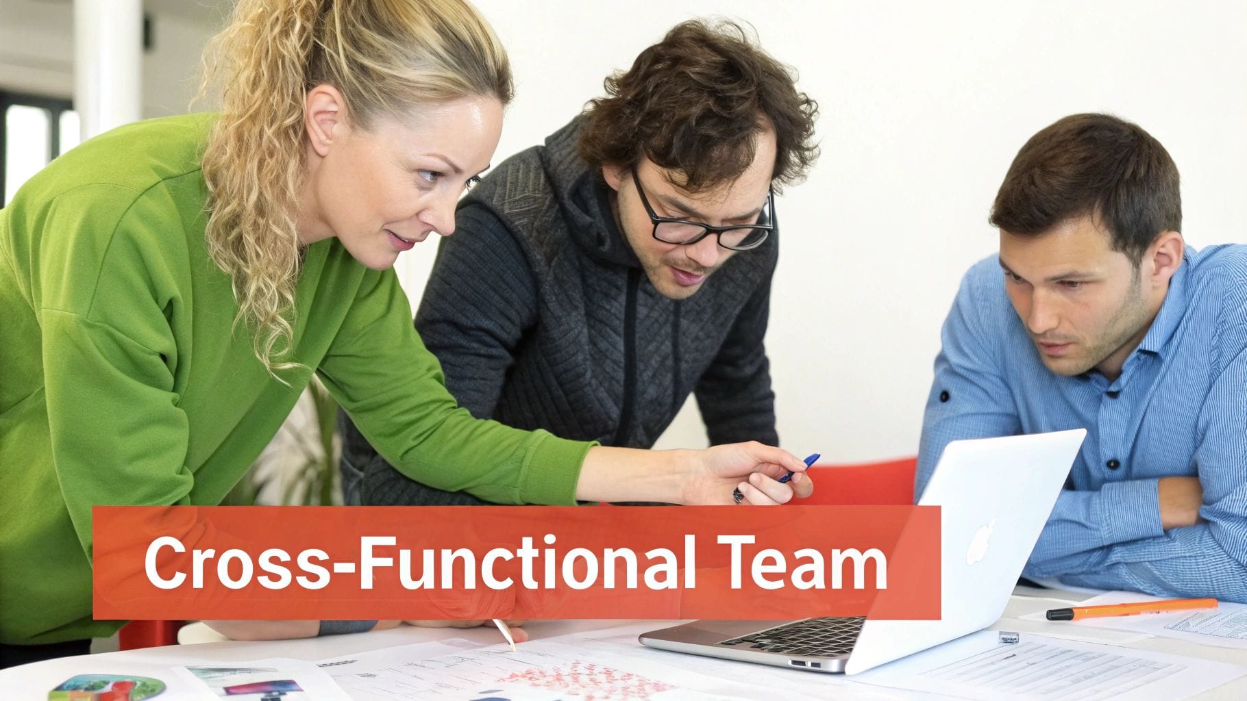 Three diverse team members collaborate around a laptop, engaged in discussion. Notes and documents are spread across a table, emphasizing teamwork in an agile design setting.