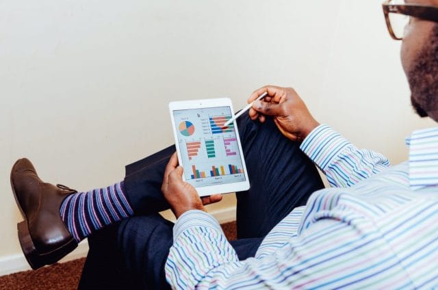 A person seated with crossed legs, holding a tablet displaying various colorful charts and graphs, wearing a striped shirt and colorful socks.