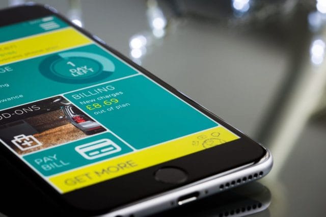 A smartphone displays a user interface with sections for usage, billing details, add-ons, and options to pay bills or get more information, set against a reflective surface.