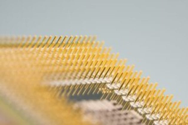 Close-up of a series of gold-plated pins on a microprocessor, showcasing their reflective surfaces and fine details against a soft background.